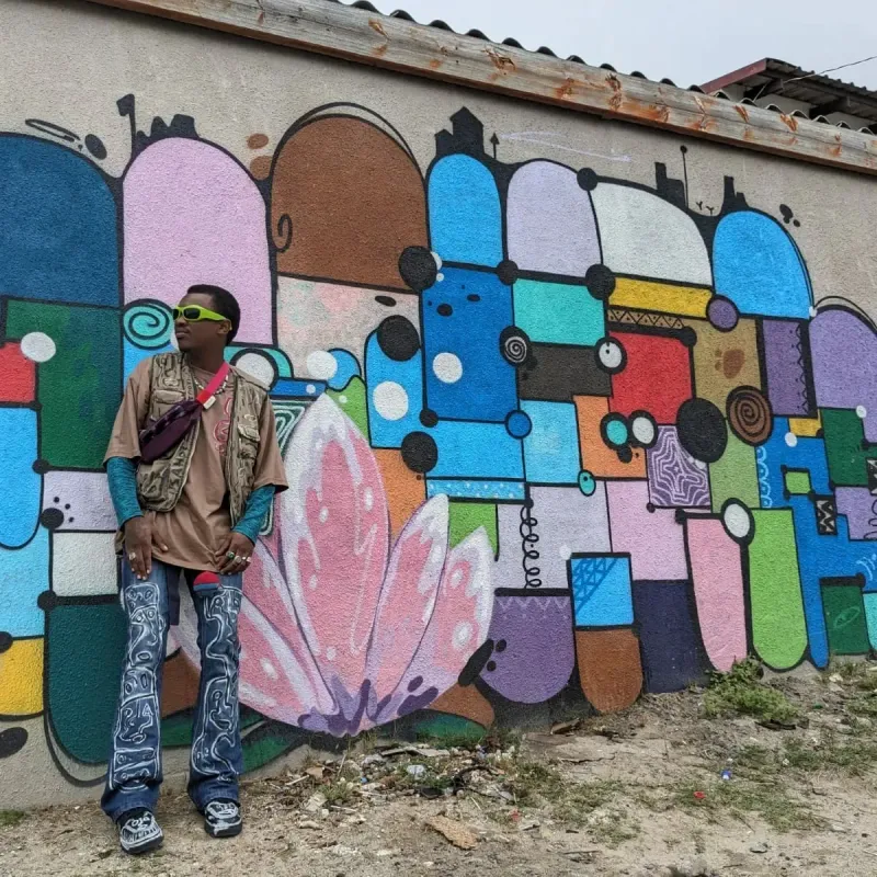 Masande in green sunglasses against a mural wall
